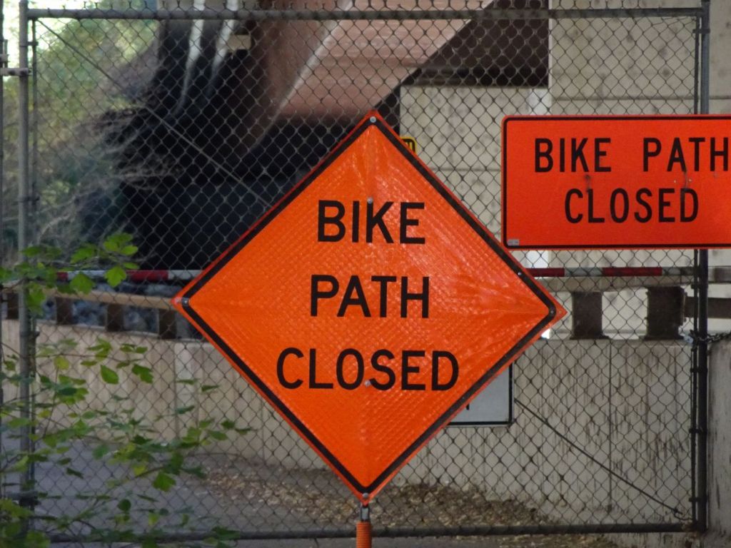 large orange "bike path closed" sign on a chain link fence