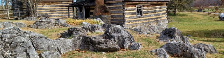 Historic log building next to creek, with ground littered with upright limestone rocks